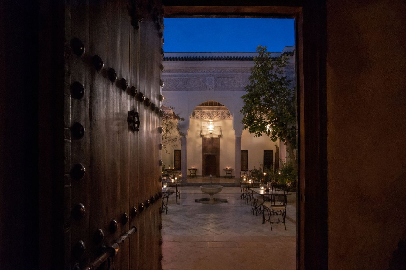 Patio de riad aux bougies et fontaine, entrevu par une porte en cèdre entrouverte au crépuscule