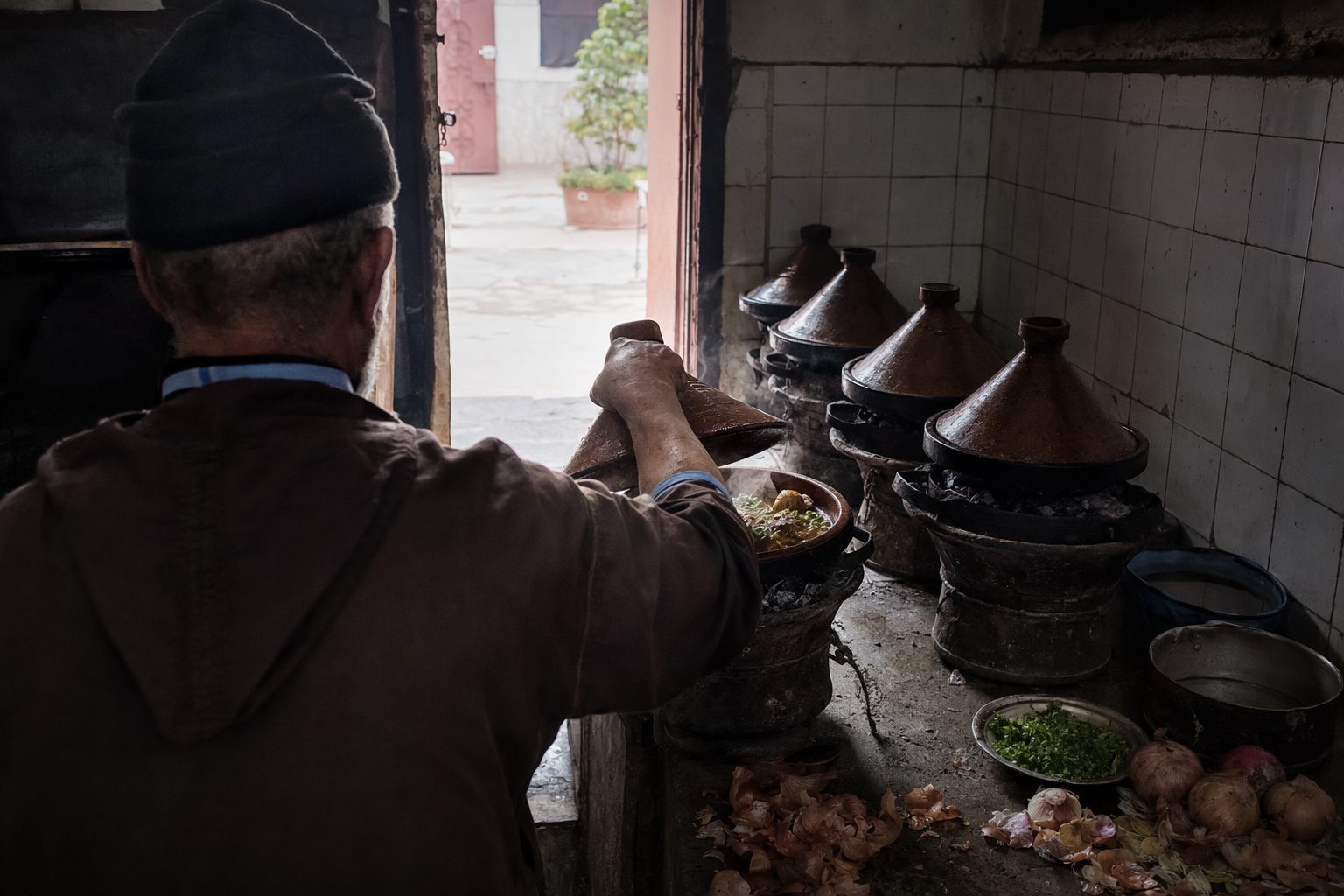 Mains d'un cuisinier soulevant le couvercle d'un tajine sur brasero dans une cuisine sombre