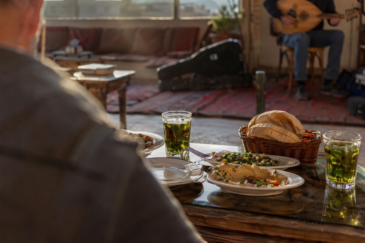Table avec thé et plats à partager, joueur de oud flou à l'arrière-plan dans la lumière du soir.