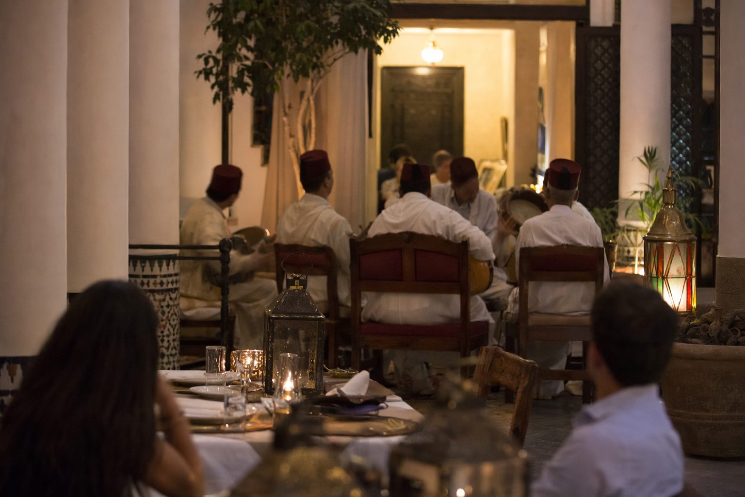 Musiciens traditionnels jouant dans le coin d'un riad le soir, tables de dîneurs au premier plan.