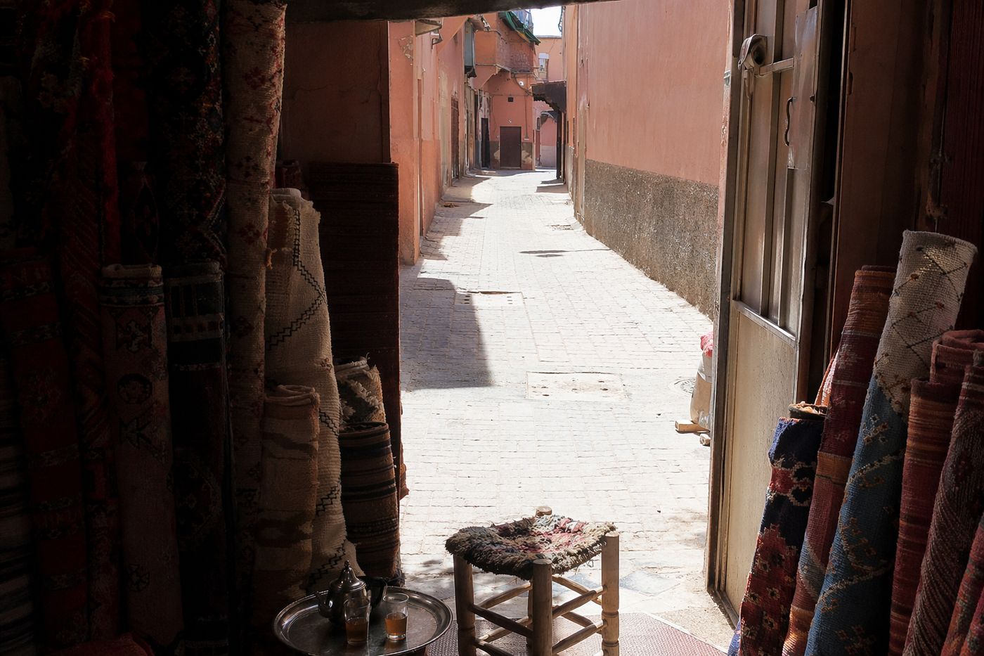 Entrée d'une boutique de tapis avec plateau à thé et deux verres posés près du seuil, ruelle en plein soleil.