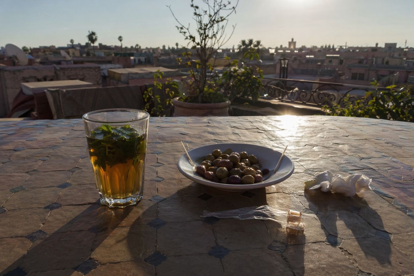 Verre de thé à la menthe et olives sur une table de rooftop, ombres longues du soleil couchant.