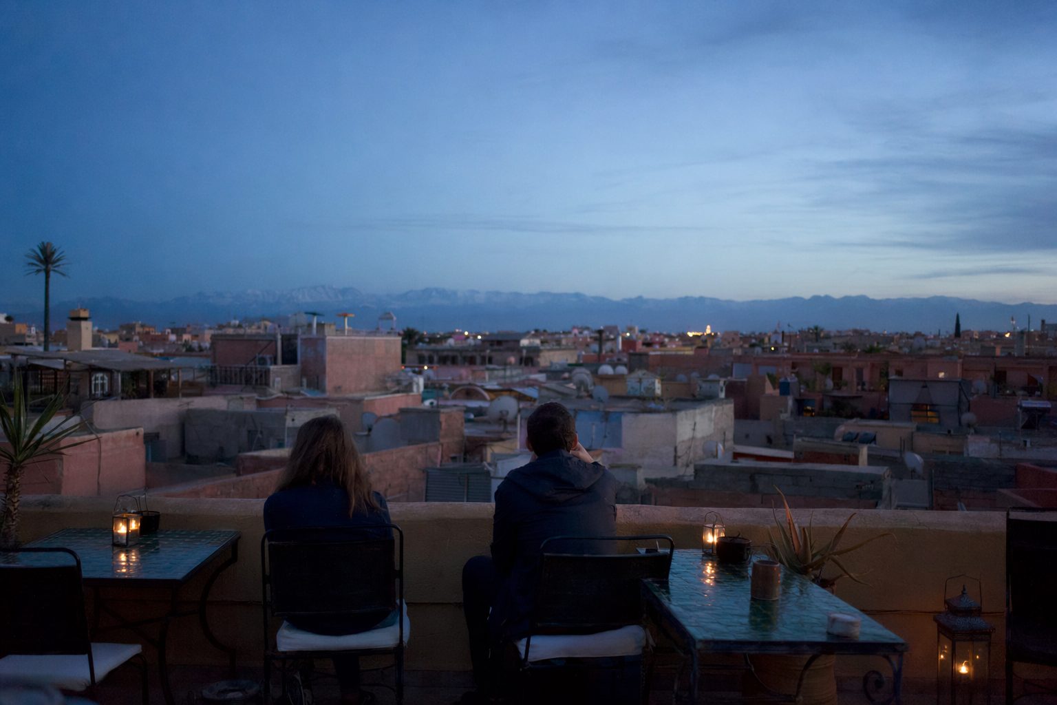 Terrasse de toit à Marrakech à l'heure bleue, tables aux bougies et toits ocre face à l'Atlas.