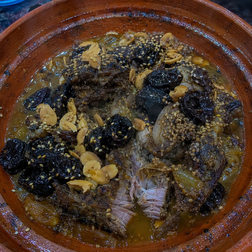 Gros plan dans un tajine d'agneau aux pruneaux, sauce au miel, sésame grillé et amandes, vapeur montante.
