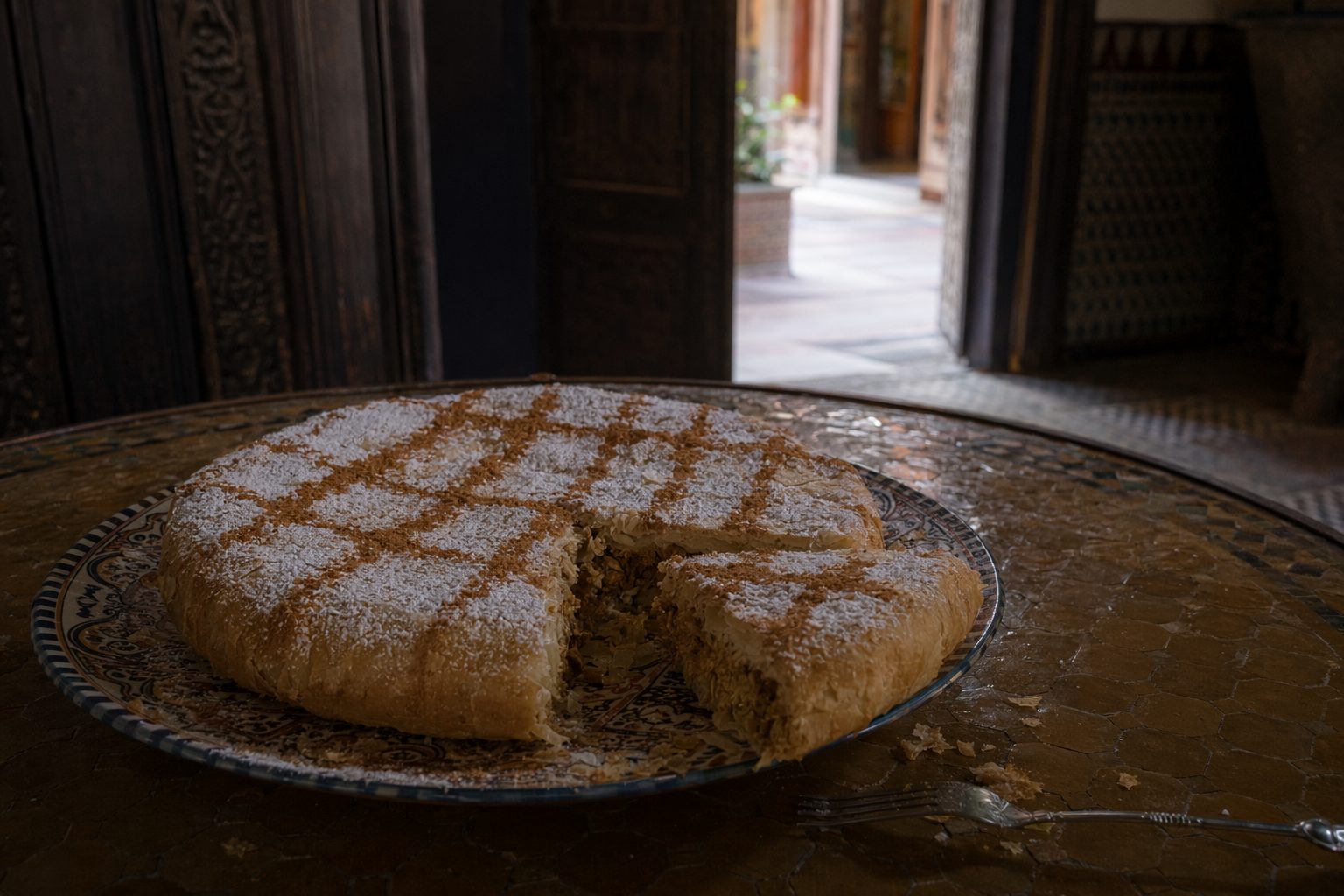 Pastilla saupoudrée de sucre glace et de cannelle, une part découpée révélant la farce aux amandes.