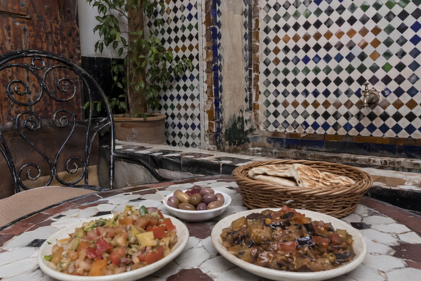 Table de café de la médina avec salades de légumes cuits, pain plat et olives sous une lumière douce et voilée.