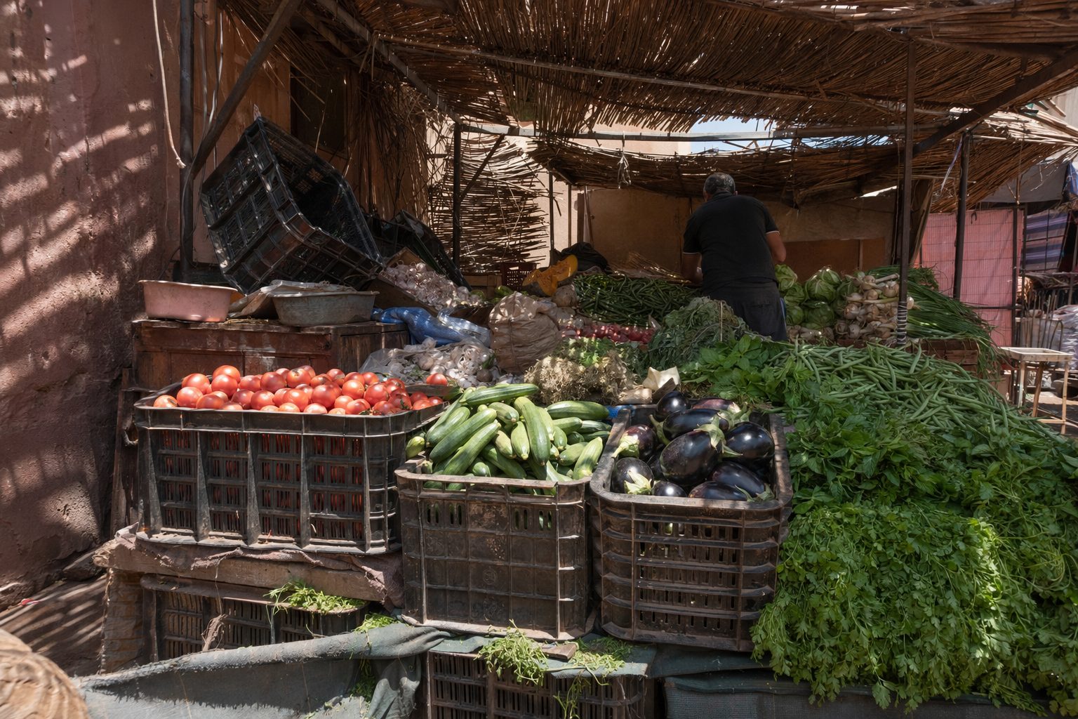 Étal de légumes dans un souk de Marrakech sous un auvent de roseaux, caisses de tomates, courgettes et herbes fraîches.
